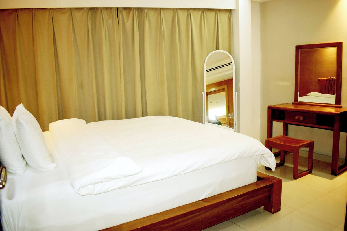 Una habitación de hotel con una cama grande, una mesita de noche de madera, un espejo y una cortina.