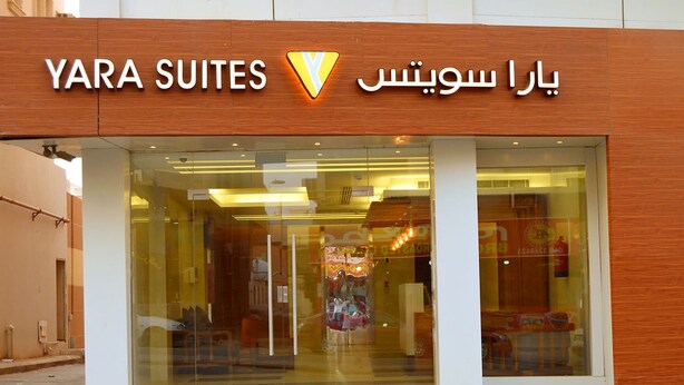 L’entrée de l’hôtel YARA SUITES, avec sa façade en verre et son revêtement extérieur en bois.