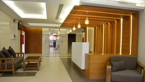 Un espace d’accueil comprenant un comptoir de réception en bois, un canapé gris et un fauteuil en bois.