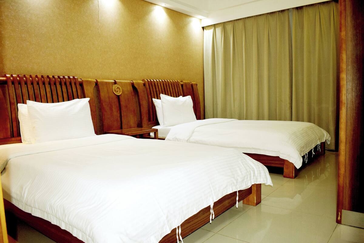 Habitación de hotel con dos camas, cabeceros de madera y un ventanal con cortinas.