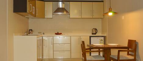 A modern kitchen with white cabinets, a stainless steel range hood, a dining table with chairs, and a hanging light fixture.