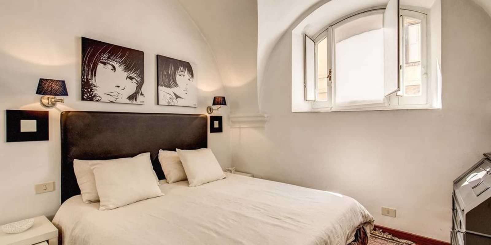 A bedroom with a large bed, two wall-mounted lamps, and a window with an open shutter.