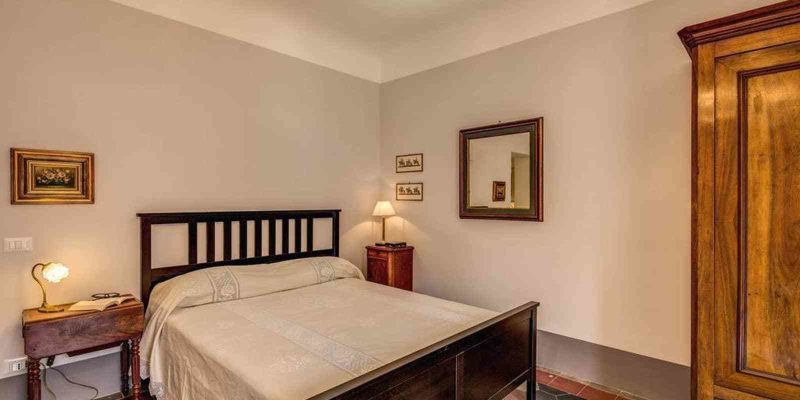 A bedroom with a bed, bedside table, lamp, and a mirror on the wall.