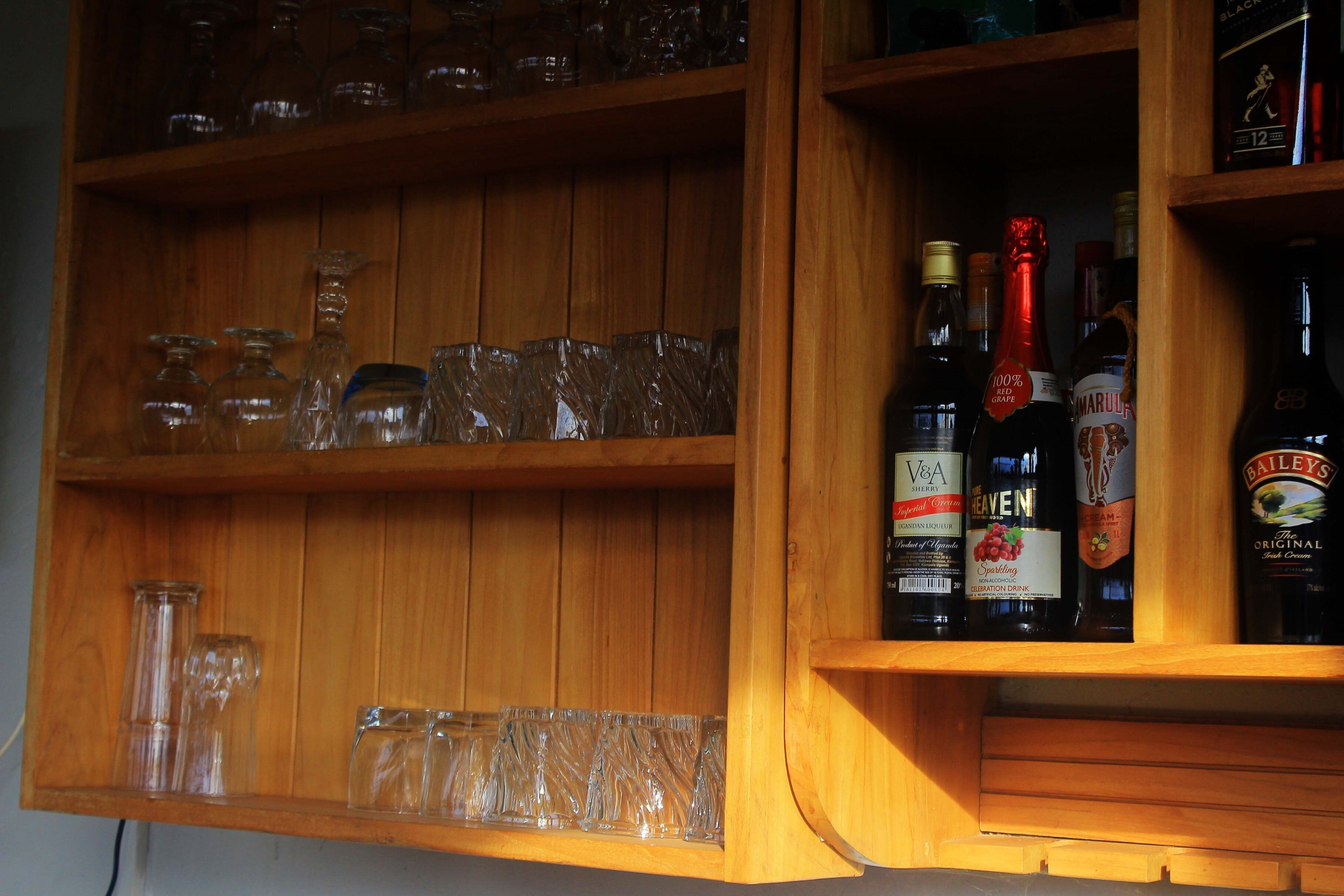 A wooden shelf with various glassware and bottles, including a bottle labeled "V&A" and another labeled "Baileys".
