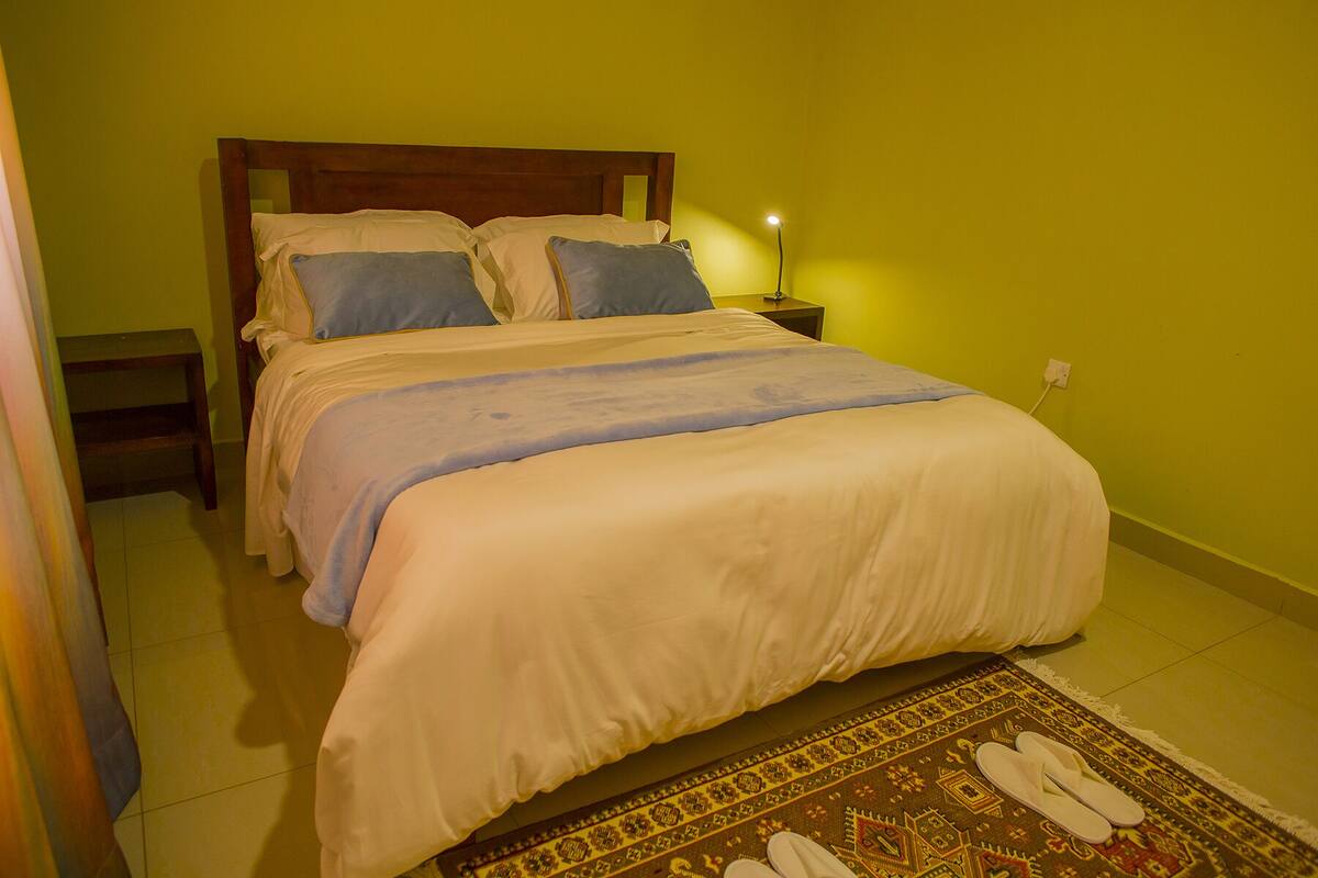 A neatly made bed with a headboard, a bedside lamp, and a patterned rug on the floor.