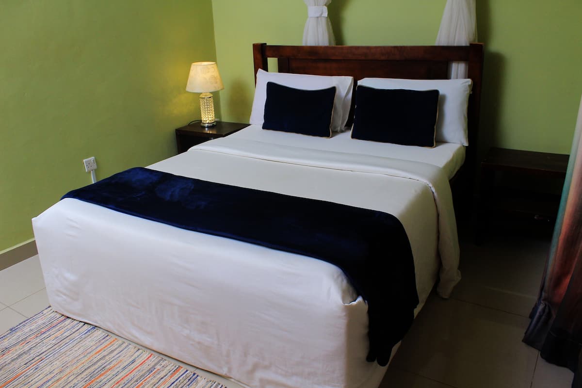 A neatly made bed with a white and blue bedspread, two pillows, and a bedside lamp on a nightstand.