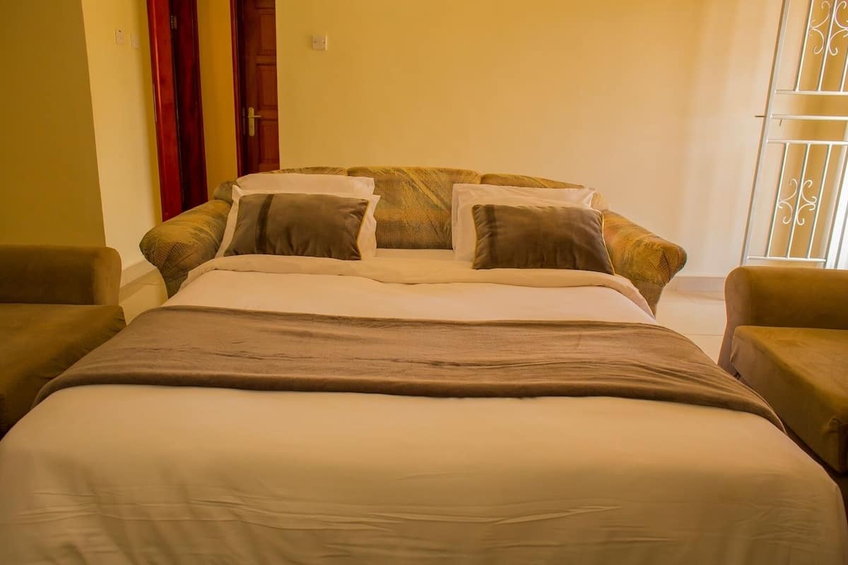A bedroom with a bed, two armchairs, and a window with a metal gate.
