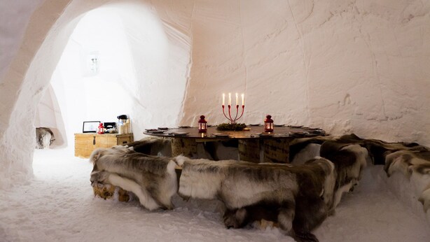Interior de una iglú con una mesa central, velas y un cofre de madera.