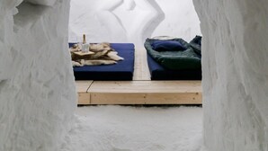 Una habitación con forma de iglú, con una cama y una pequeña mesa con una botella.
