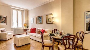 A cozy living room with a white sofa, a dining table set for four, and a radiator. - Roma Barocca Spanish Steps (Rome)