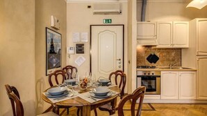A dining area with a wooden table set for four, surrounded by chairs. There is a kitchen with white cabinets and a stove. - Roma Barocca Spanish Steps (Rome)