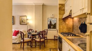 A dining area with a wooden table and chairs, a white sofa, and a kitchen with a gas stove and cabinets. - Roma Barocca Spanish Steps (Rome)