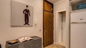 Une pièce avec une porte en bois, un réfrigérateur blanc et une œuvre d’art accrochée au mur représentant un homme en costume.