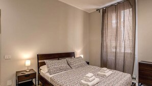 Une chambre d’hôtel avec un lit, une table de chevet, une lampe et une fenêtre avec des rideaux.