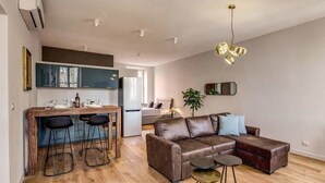 Una sala de estar moderna con un sofá de cuero, un comedor con taburetes de bar y una cocina con refrigerador.