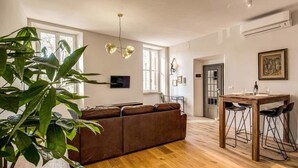 Un espacio moderno para vivir con piso de madera, un sofá marrón, una mesa de comedor con taburetes altos y una planta grande.