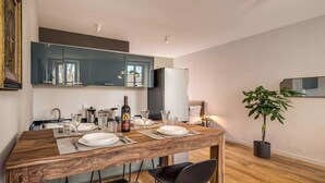 Comedor con mesa de madera dispuesta para cuatro personas, un espejo grande arriba y una planta en maceta al lado.