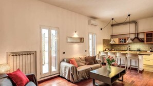A modern living room with a sofa, a coffee table, and a dining area with bar stools. There is a kitchen with a stove and cabinets. - Attic terrace with St Peter's Dome View (Rome)