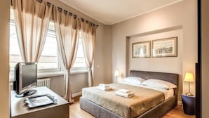 Une chambre à coucher avec un lit, des lampes de chevet, un bureau avec un ordinateur et des rideaux.