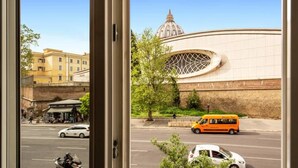Une vue à travers une fenêtre donnant sur une rue, avec un grand bâtiment doté d’un dôme et d’une fenêtre circulaire.