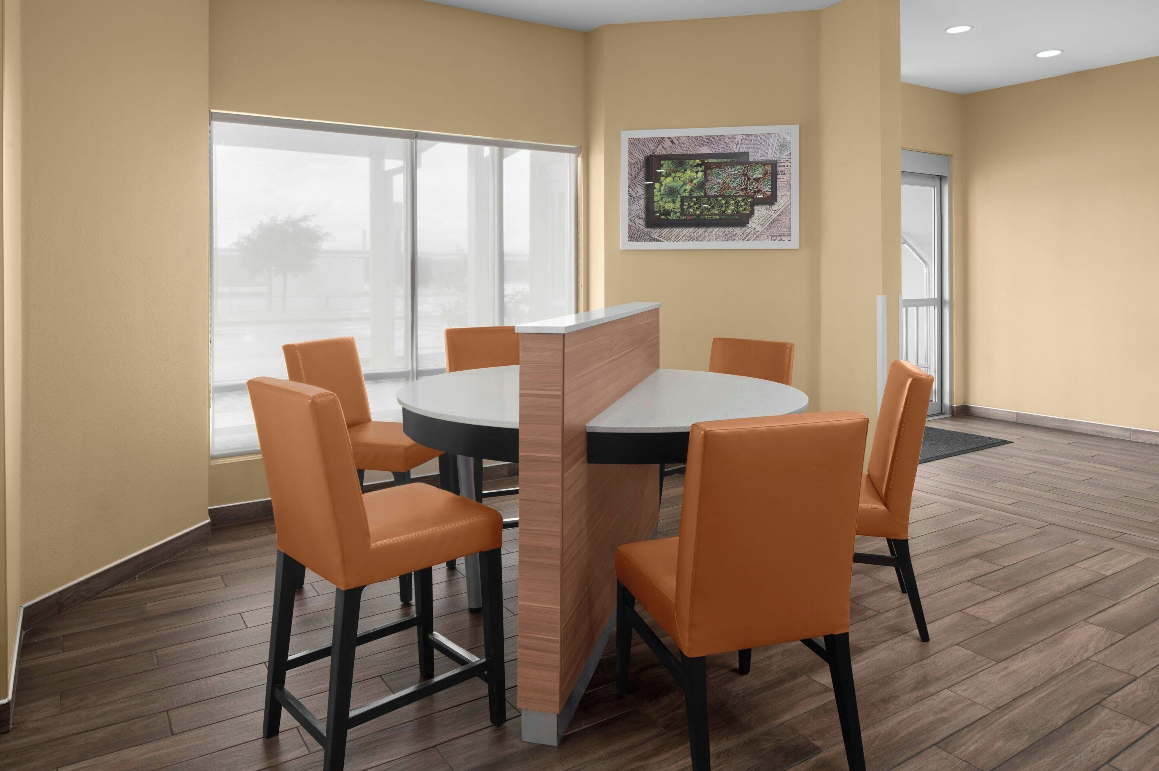 Un salón de conferencias con una mesa redonda, seis sillas color naranja, un separador de madera y un amplio ventanal con vistas.