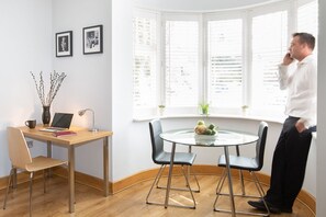 A modern room with a wooden desk, two chairs, a laptop, a vase with branches, and a window with blinds. - HomefromHolme Alban House (St Albans)