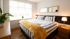 A neatly arranged bedroom with a bed, bedside tables, a lamp, a potted plant, and a window with blinds. - HomefromHolme Alban House (St Albans)