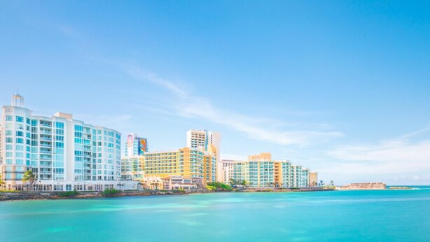 Un hotel frente al mar con varios edificios altos, un cielo azul despejado y aguas turquesas.