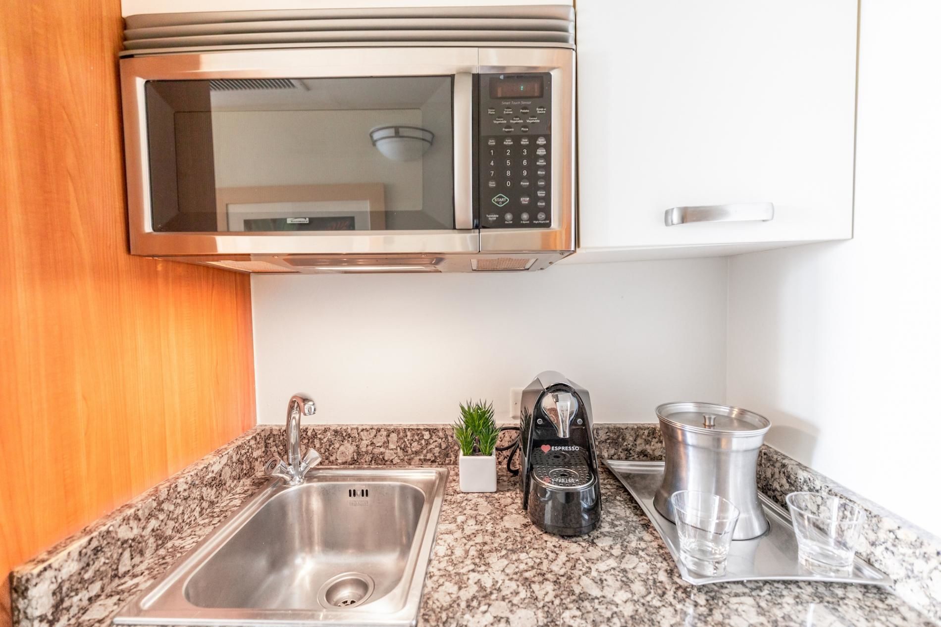 A kitchen with a stainless steel sink, a coffee machine, a microwave, and a small potted plant.