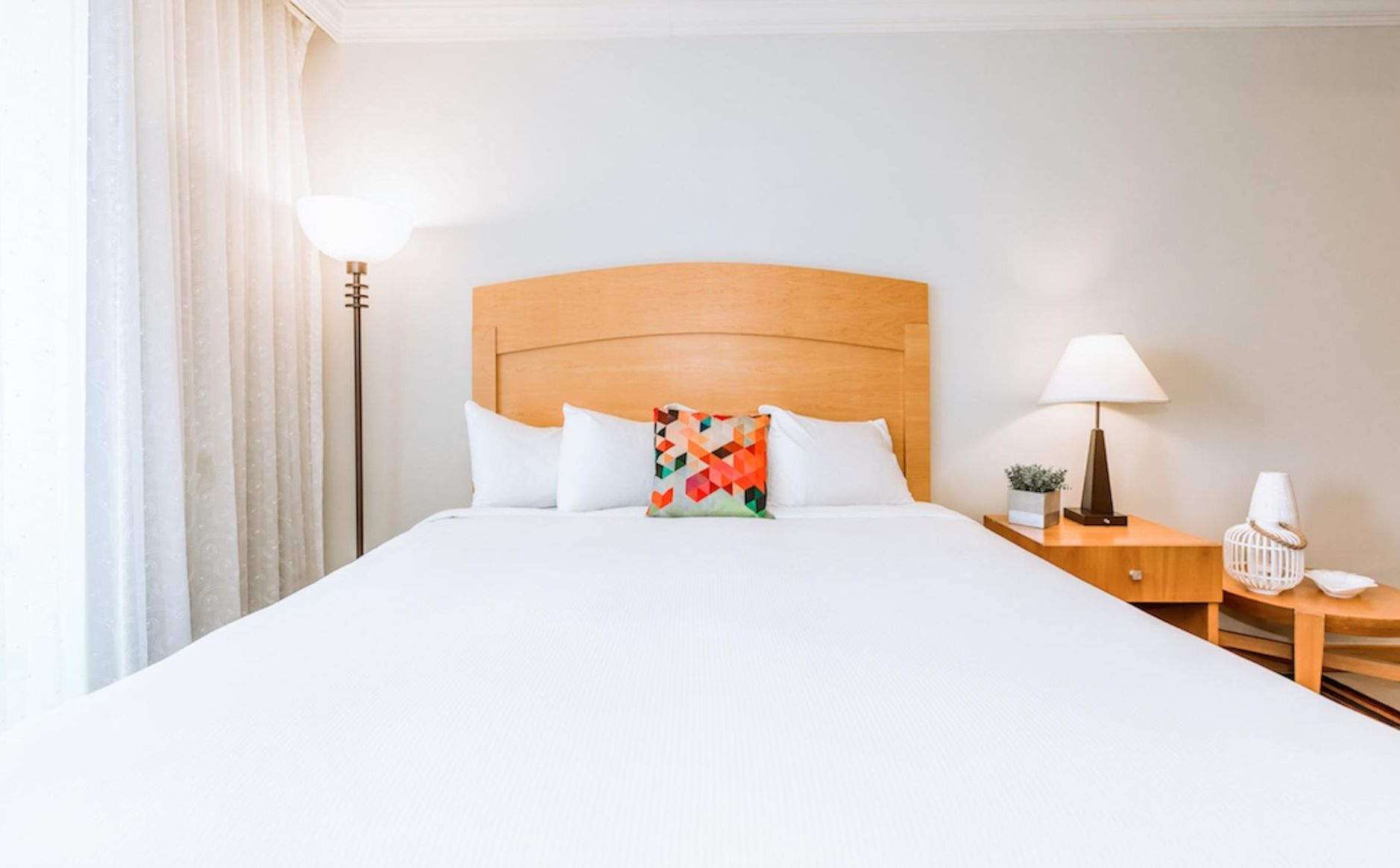 Una camera d'albergo con un letto grande, una testiera in legno, due comodini con lampade e una finestra con tende.