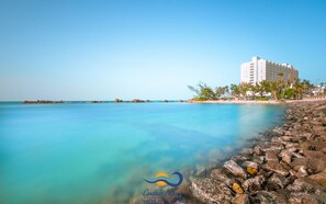 A coastal hotel with a clear view of the ocean, a rocky shoreline, and a building with multiple floors. - Condado Lagoon Hospitality (San Juan)