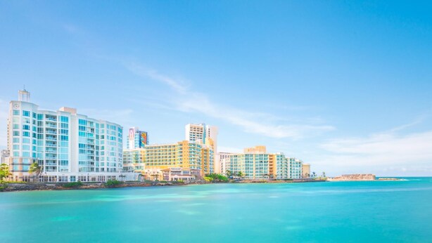 A coastal hotel with multiple high-rise buildings, a clear blue sky, and turquoise waters. - 524 Ocean Studio (San Juan)
