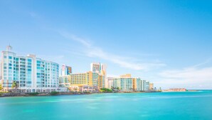 A coastal hotel with multiple high-rise buildings, a clear blue sky, and turquoise waters. - 510 Ocean Studio (San Juan)