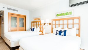 A hotel room with two beds, a wooden headboard, a wall-mounted air conditioner, and a framed artwork. - 510 Ocean Studio (San Juan)