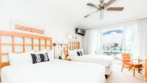 A hotel room with two beds, a ceiling fan, a TV, a balcony with a view of the city, and a dining area with a chair. - 619 Breezy Studio (San Juan)