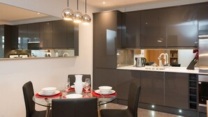 A modern kitchen with dark cabinetry, a glass dining table, and a built-in island with a sink and appliances. - HomefromHolme St Peters Mews (St Albans)