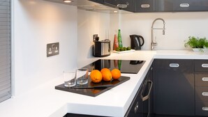 A modern kitchen with black cabinets, a white countertop, a coffee maker, a kettle, a sink, and a potted plant. - HomefromHolme St Peters Mews (St Albans)