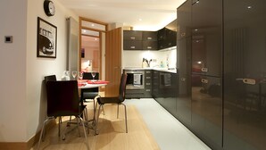 A modern kitchen with black cabinets, a refrigerator, and a dining area with a table and chairs. - HomefromHolme St Peters Mews (St Albans)