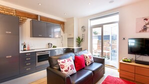 A modern kitchen with grey cabinets, a flat-screen TV, and a red rug. - HomefromHolme St Peters Mews (St Albans)