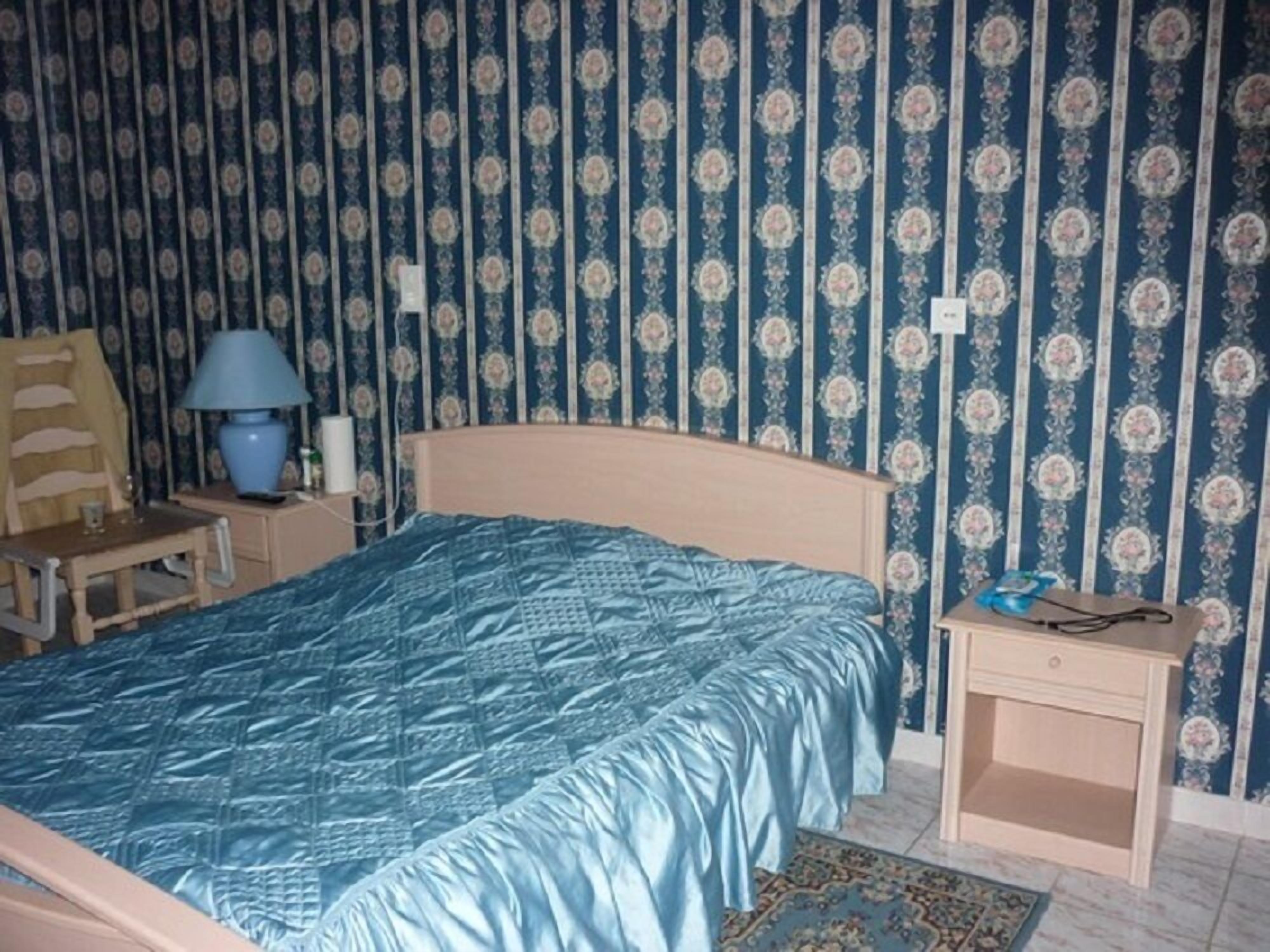 Un dormitorio con cama, mesita de noche, una silla y una lámpara.