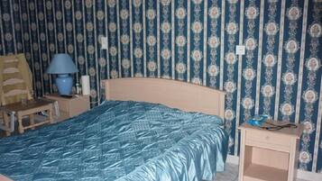 Een slaapkamer met een bed, nachtkastje, stoel en lamp.