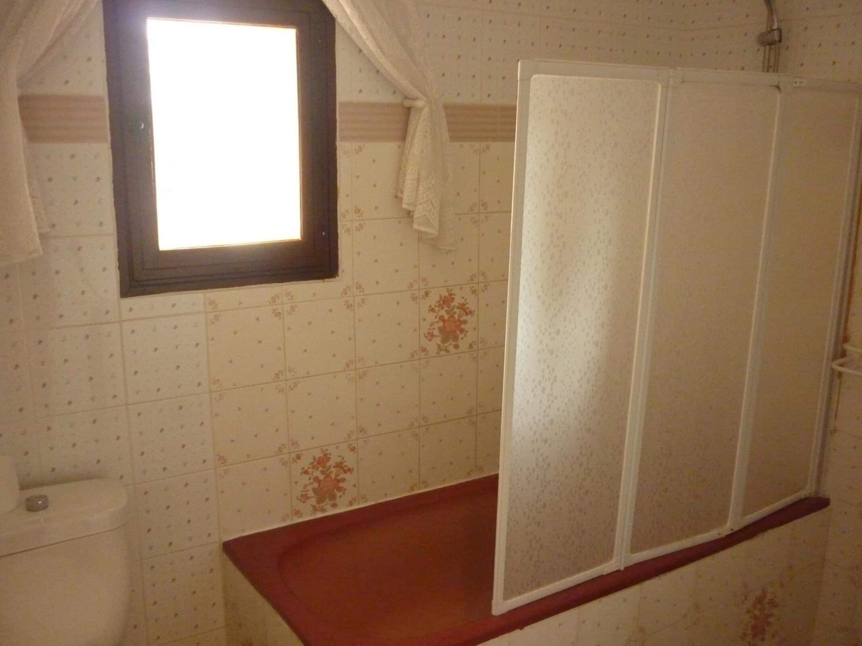 A bathroom with a window, a shower enclosure, and a toilet.