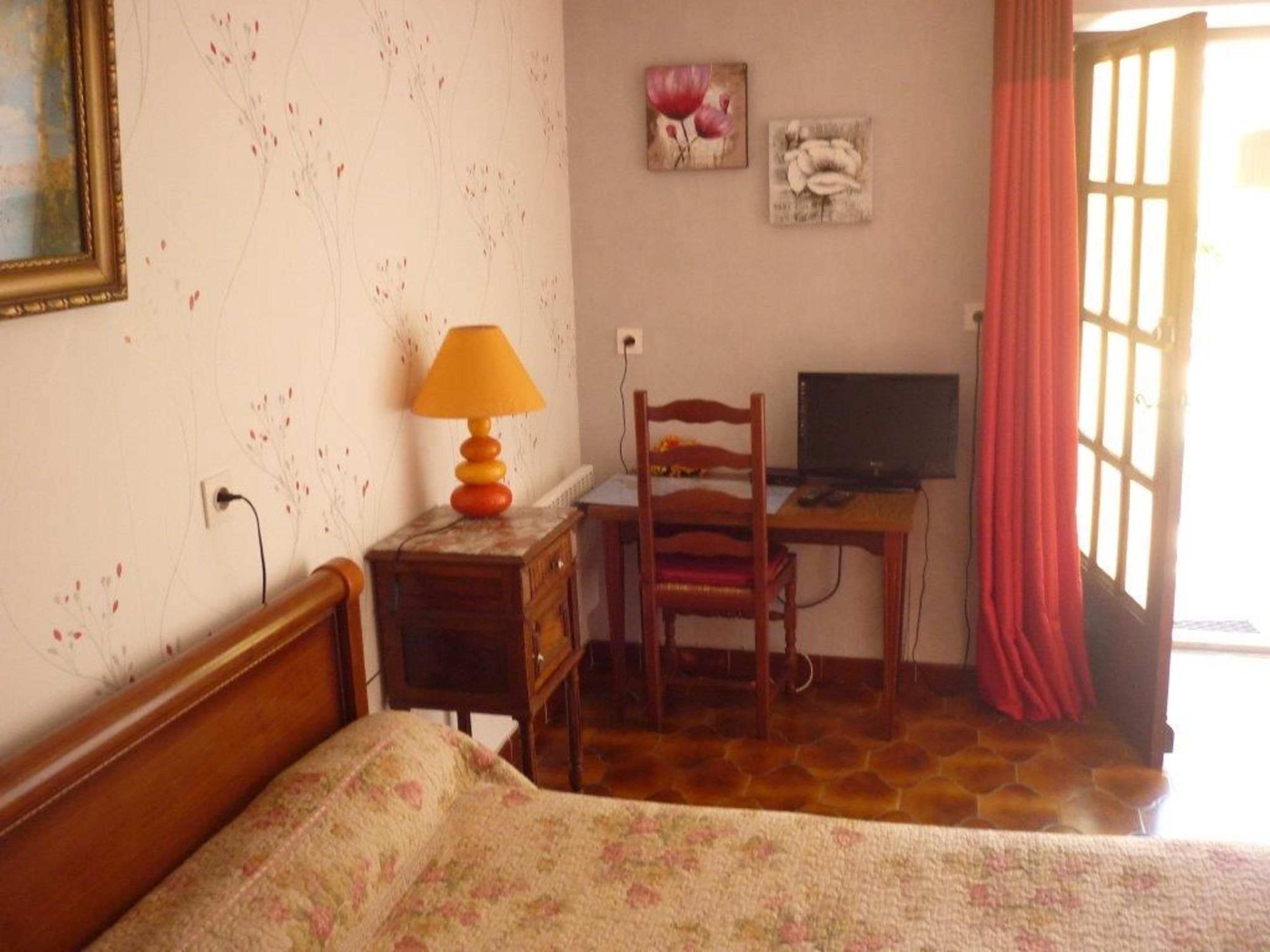 A bedroom with a bed, a desk with a computer, a chair, a lamp, and a window with curtains.
