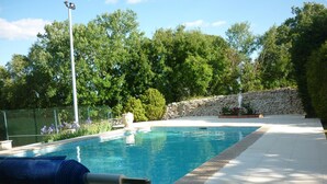A swimming pool with a stone wall and a metal fence in the background. - Domaine de la Rode Buze (Cahors)