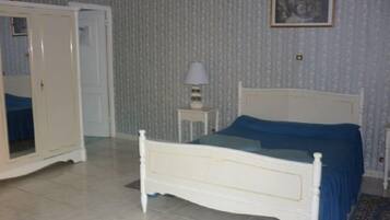 Un dormitorio con cama blanca, colcha azul, armario blanco, mesita de noche pequeña con lámpara y pared con diseño.