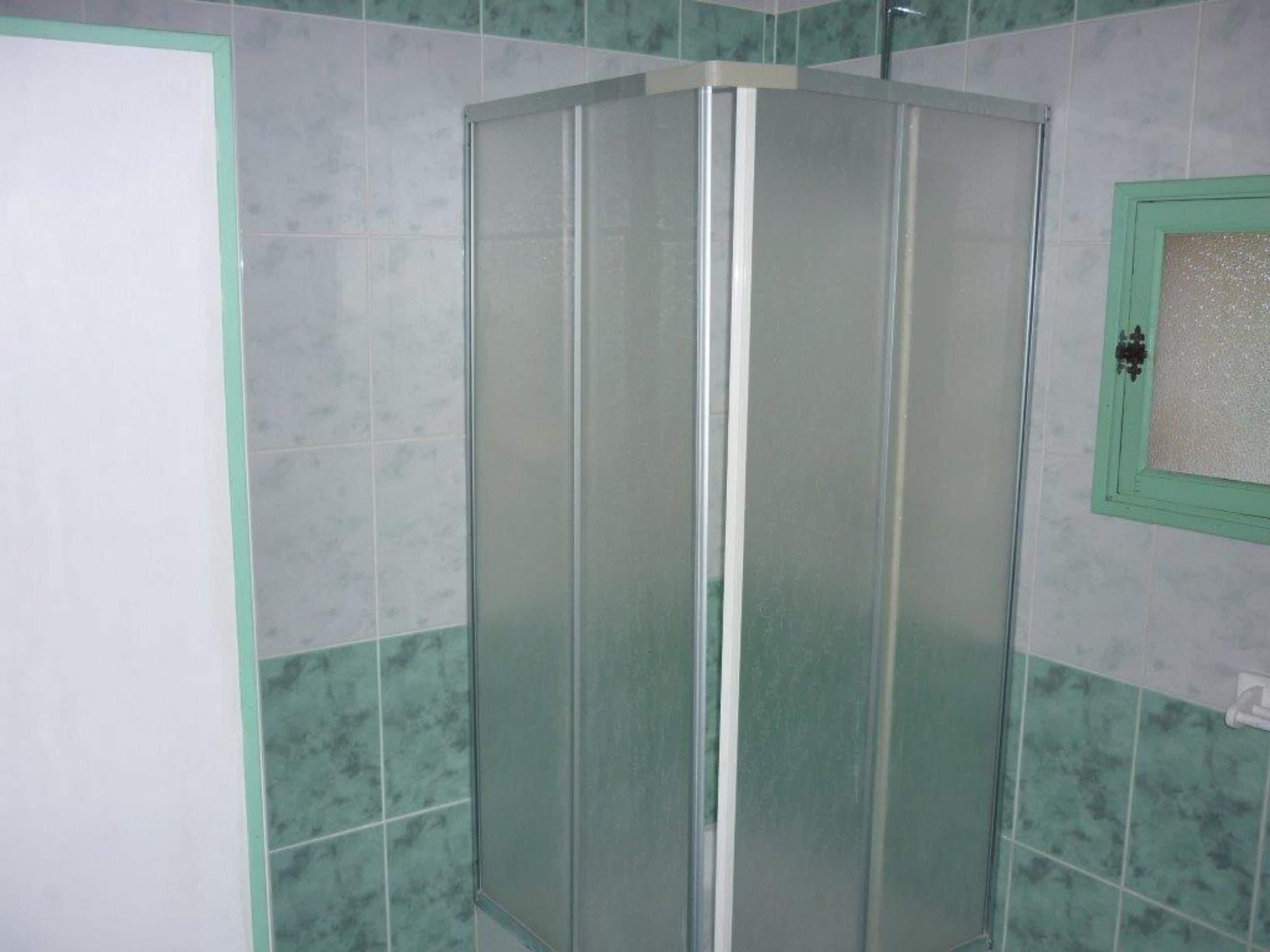 A glass-enclosed shower stall with a green frame, tiled walls, and a white door.