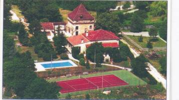 Vista aérea de una propiedad con un edificio central, una piscina y canchas de tenis.