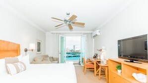 A hotel room with a bed, a desk, a TV, a ceiling fan, and a view of a body of water. - 825 SEA & SUN Suite (San Juan)
