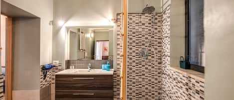 A modern bathroom with a large mirror, a wooden vanity, a shower with a checkered tile wall, and a window.