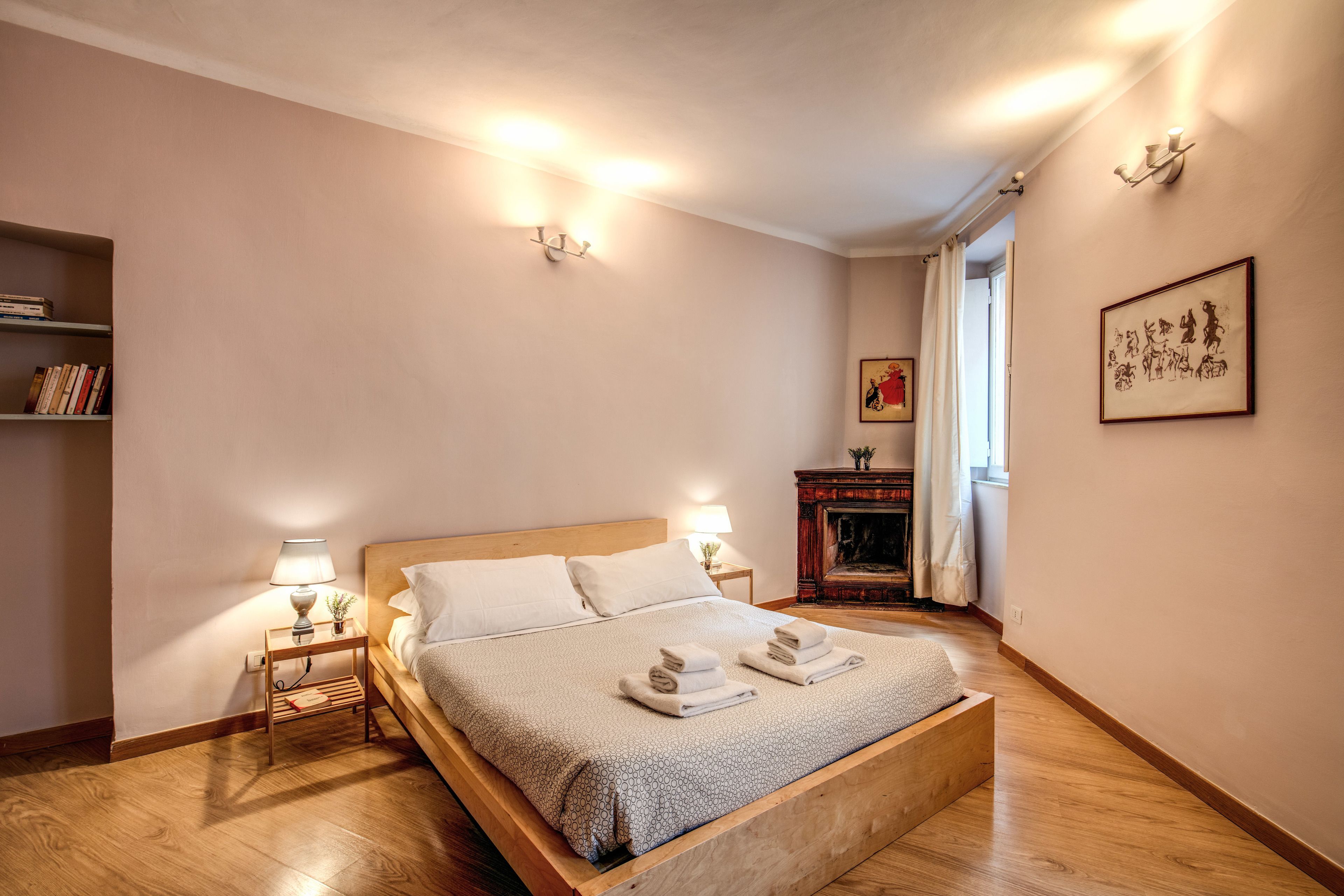 Un dormitorio ordenado con una cama de madera, lámparas de noche, una estantería y una chimenea.